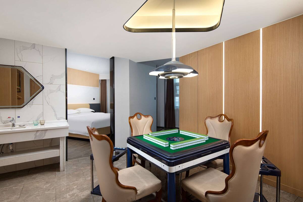 Une chambre d’hôtel comprenant un lit, un bureau avec un miroir, une table à manger avec des chaises et un luminaire au plafond.