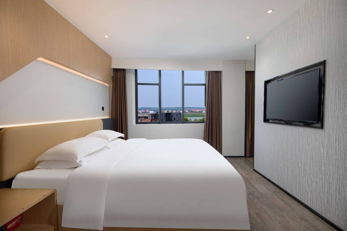 Une chambre d’hôtel avec un grand lit, un téléviseur fixé au mur et une fenêtre donnant sur la ville.
