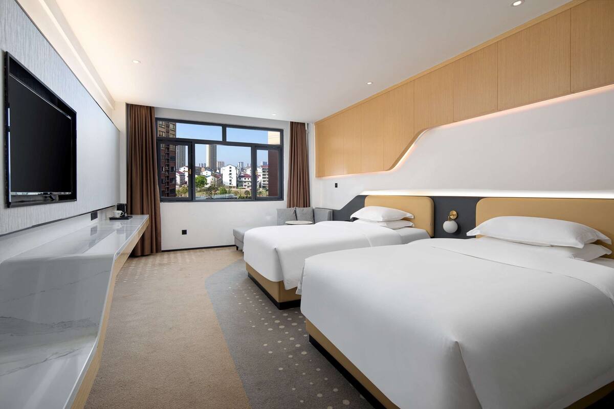 Une chambre d’hôtel avec deux lits, une télévision, un bureau et une grande fenêtre donnant sur la ville.