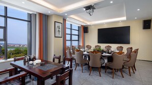 A dining area with a large table and multiple chairs, a projector screen on the wall, and a view of the outdoors through large windows. - Microtel by Wyndham Miluo Downtown Hotel (Yueyang)