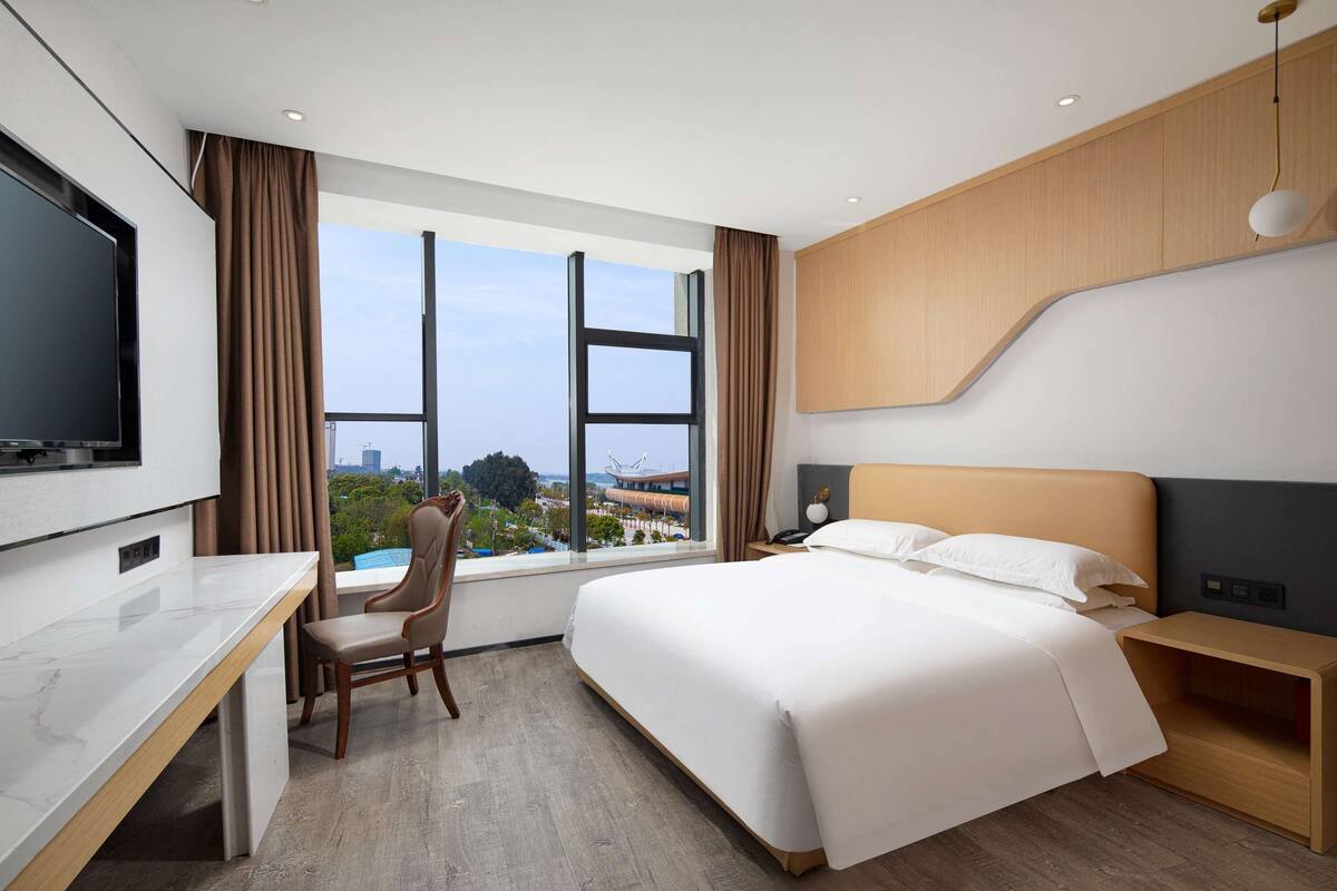 Une chambre d’hôtel avec un grand lit, un bureau, une chaise, une télévision et une fenêtre donnant sur la ville.
