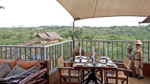 Un coin repas avec une table dressée pour quatre personnes, donnant sur un paysage verdoyant, avec des arbres et un bâtiment situé au loin.