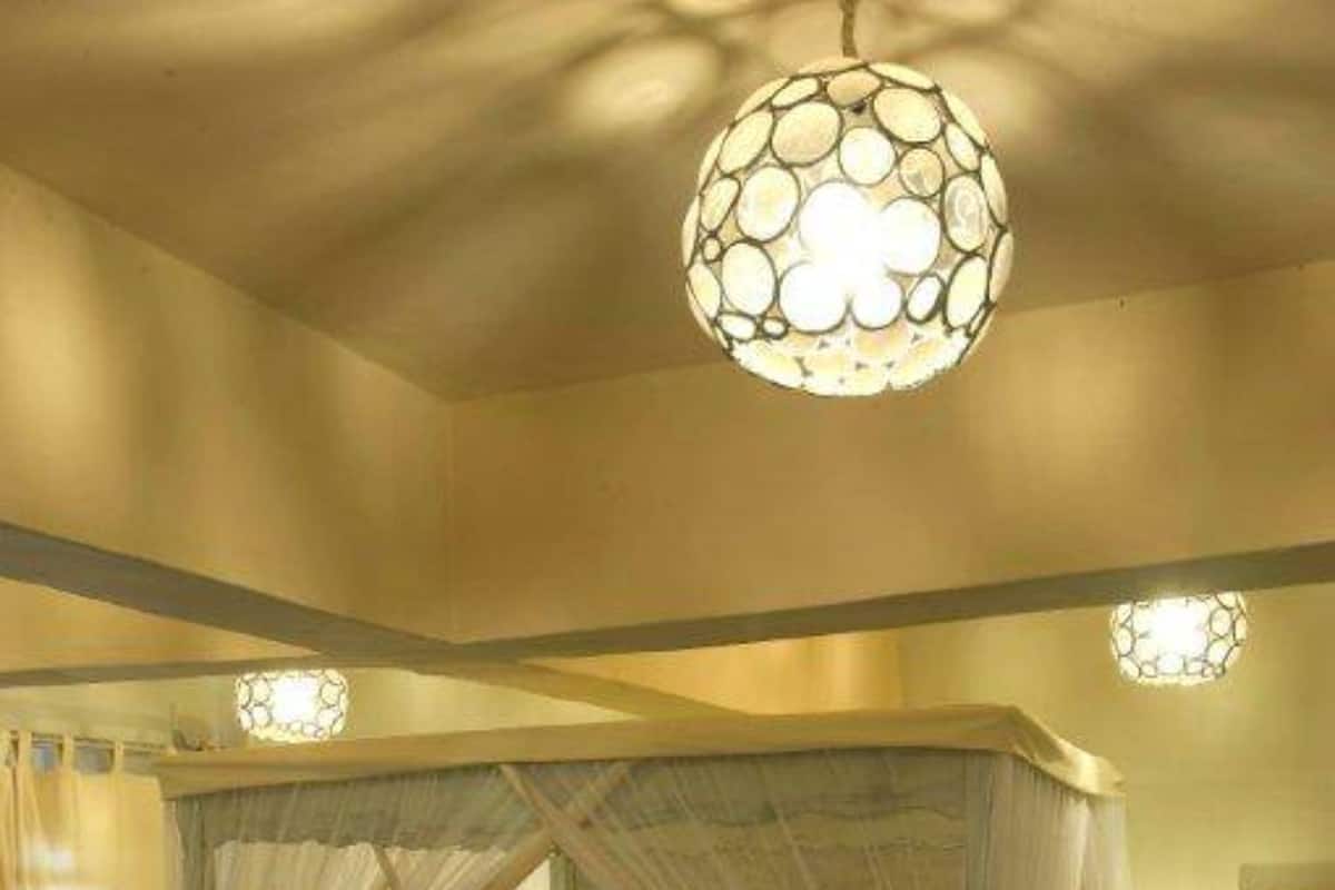 Un lit à baldaquin à quatre poteaux, recouvert d’une courtepointe blanche et agrémenté de nombreux coussins, un tapis à motifs et un luminaire suspendu.