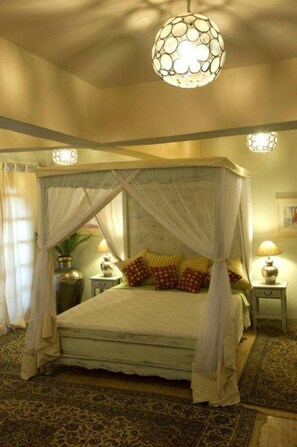 A four-poster canopy bed with a white bedspread and multiple pillows, a patterned rug, and a hanging light fixture. - Rolf's Place (Nairobi)
