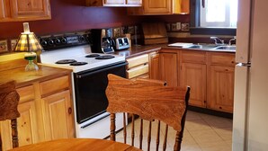 A kitchen with wooden cabinets, a stove, a refrigerator, and a dining table with a chair. - LOVELY/CENTRALLY LOCATED/GROUND FLOOR APARTMENT (Warrensburg)