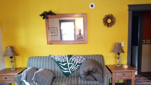 A living room with a yellow wall, a wooden sofa, two side tables, a coffee table, and a patterned rug. - LOVELY/CENTRALLY LOCATED/GROUND FLOOR APARTMENT (Warrensburg)