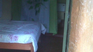 Um quarto com pouca luz, uma cama, uma mesinha de cabeceira e um abajur.