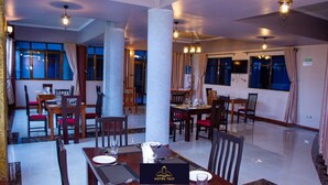 A hotel dining area with multiple tables and chairs, large windows, and a modern ceiling design. - Hotel Taji (Nanyuki)