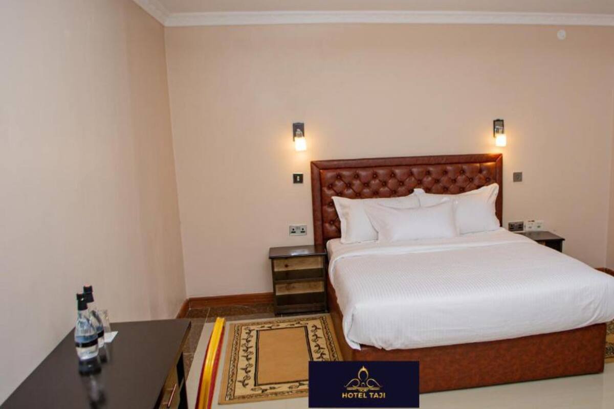 A hotel room with a large bed, two bedside tables, a nightstand, a water bottle, and a decorative rug.