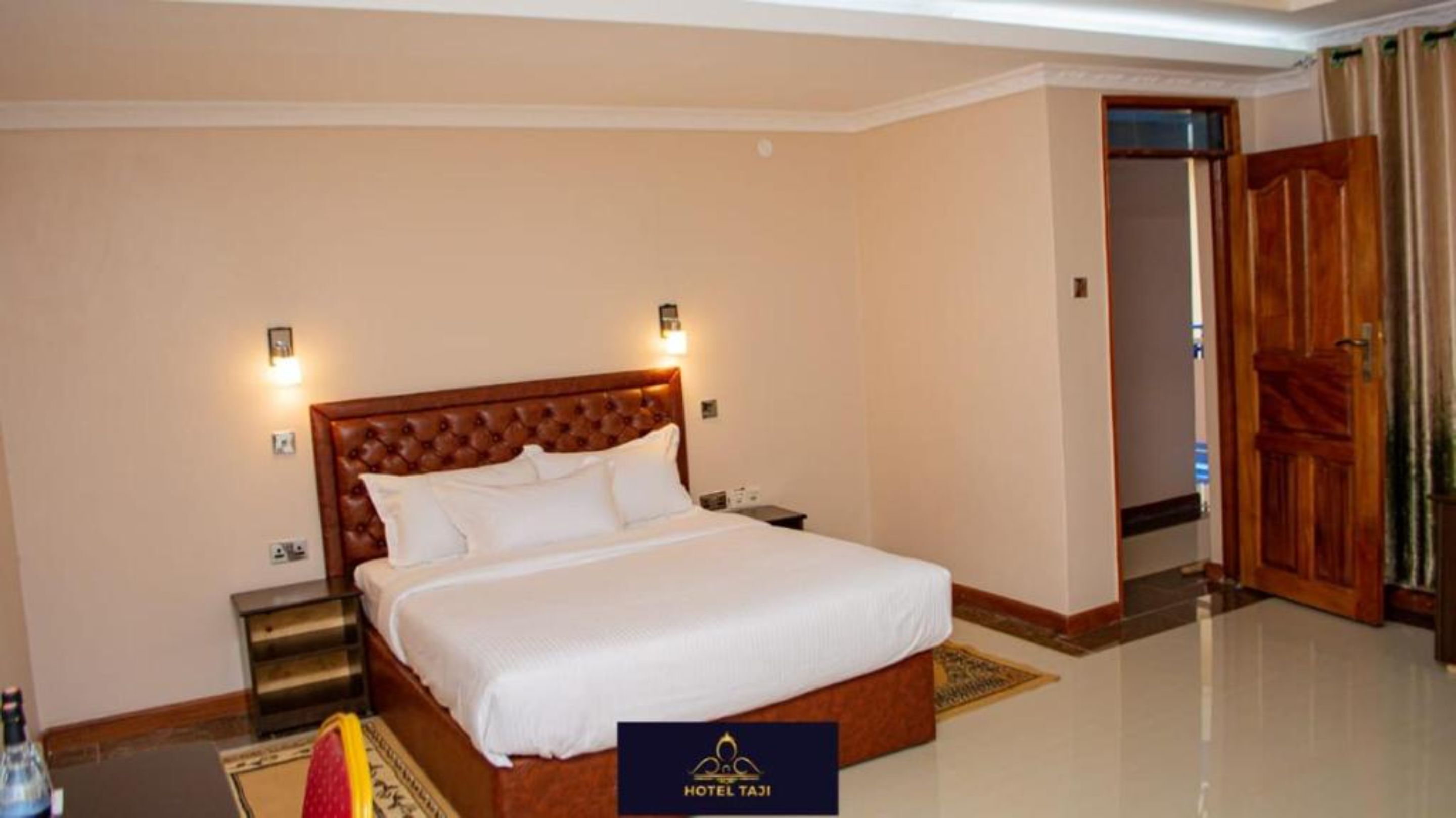 A hotel room with a large bed, two bedside lamps, a nightstand, and a wooden door.