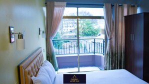 A hotel room with a bed, a window with curtains, a view of the outside, and a door. - Hotel Taji (Nanyuki)