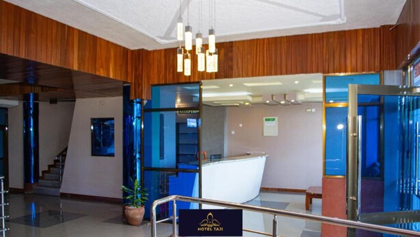 A modern hotel lobby with a reception desk, a staircase, and a potted plant. - Hotel Taji (Nanyuki)