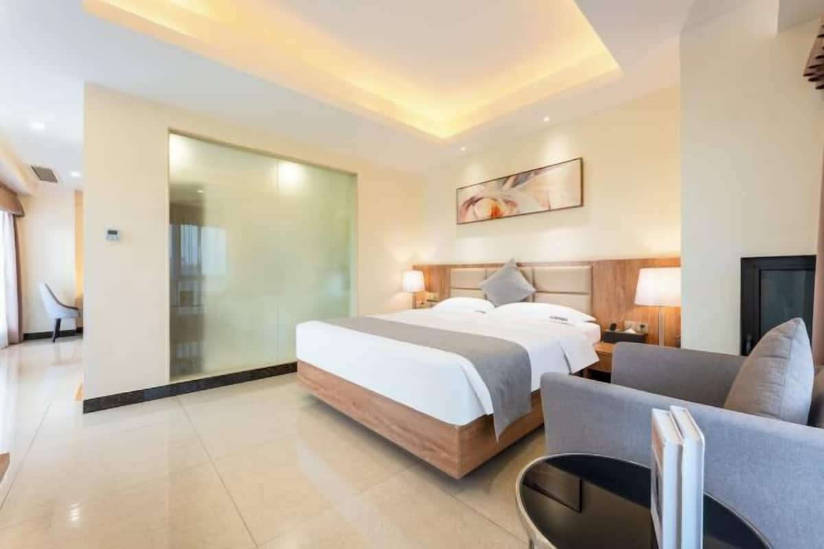 A modern hotel room with a large bed, a sofa, a desk, and a glass partition.