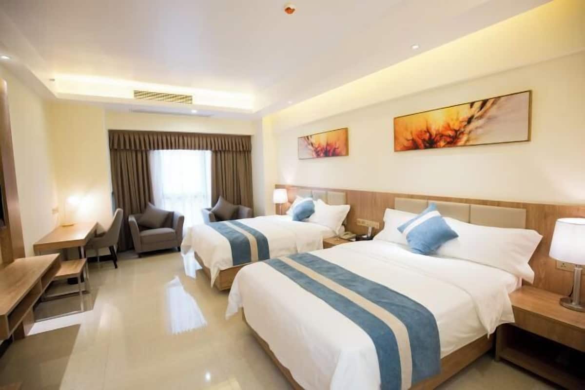 A hotel room with two beds, a desk, a chair, and a window with curtains.