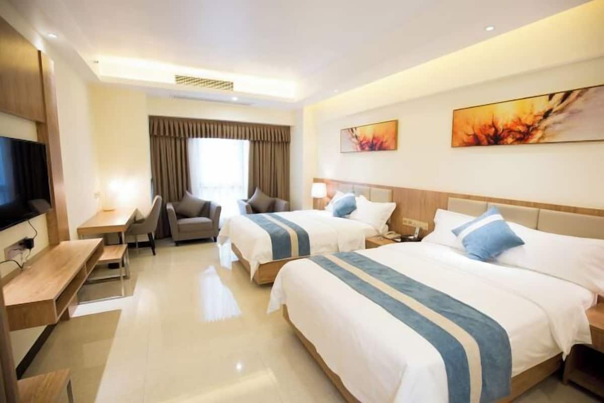 A hotel room with two beds, a desk, a chair, a TV, and artwork on the walls.