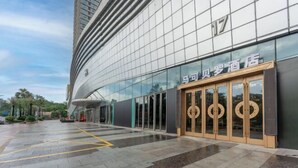 Une entrée d’hôtel moderne avec une façade en verre et une porte en bois ornée de motifs circulaires.
