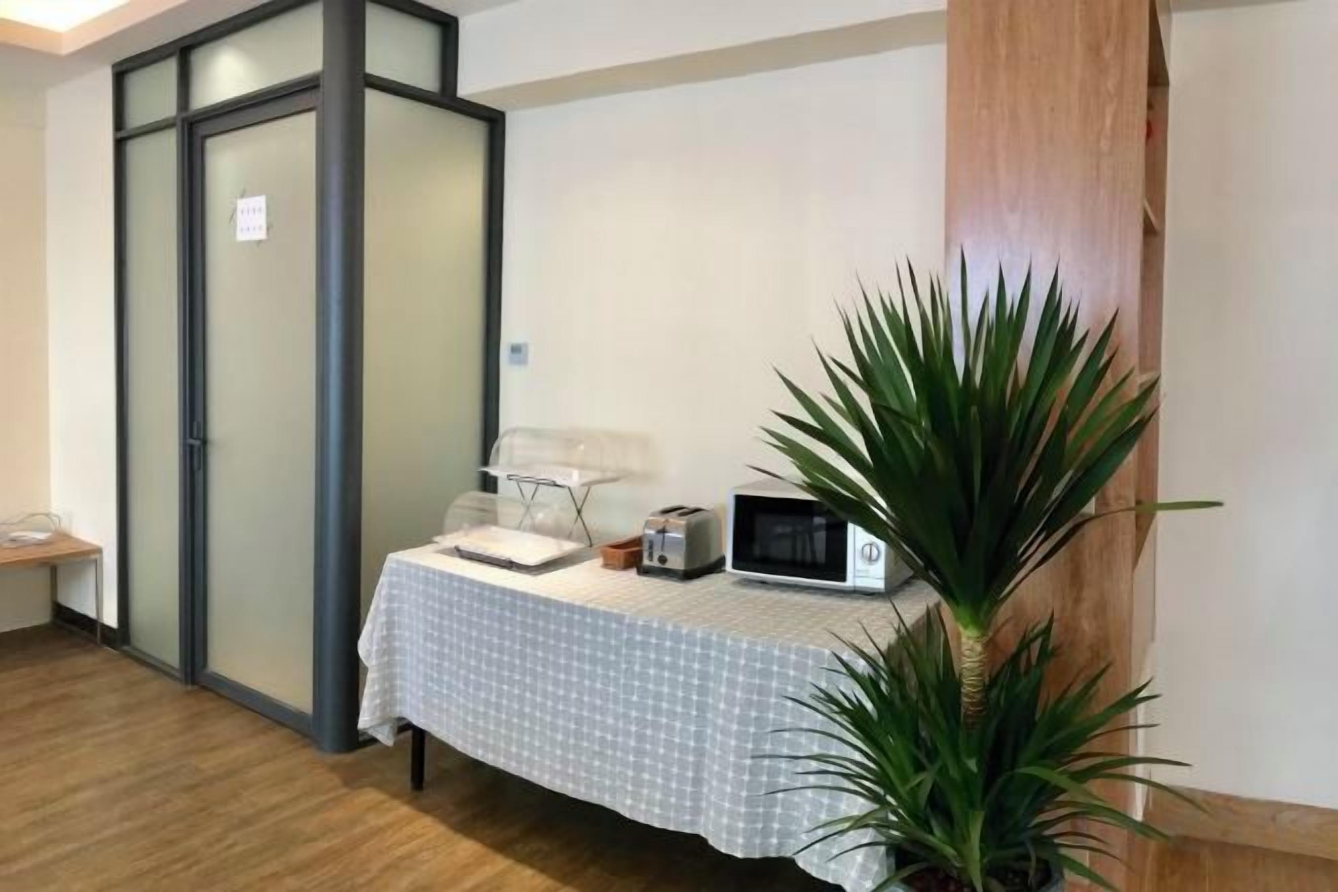 A room with a bed, a bedside table, a microwave, and a potted plant.
