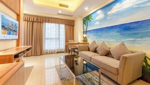 Un salon moderne avec un canapé beige, une table basse et un téléviseur posé sur un meuble en bois. Un grand tableau représentant une scène de plage est accroché au mur.