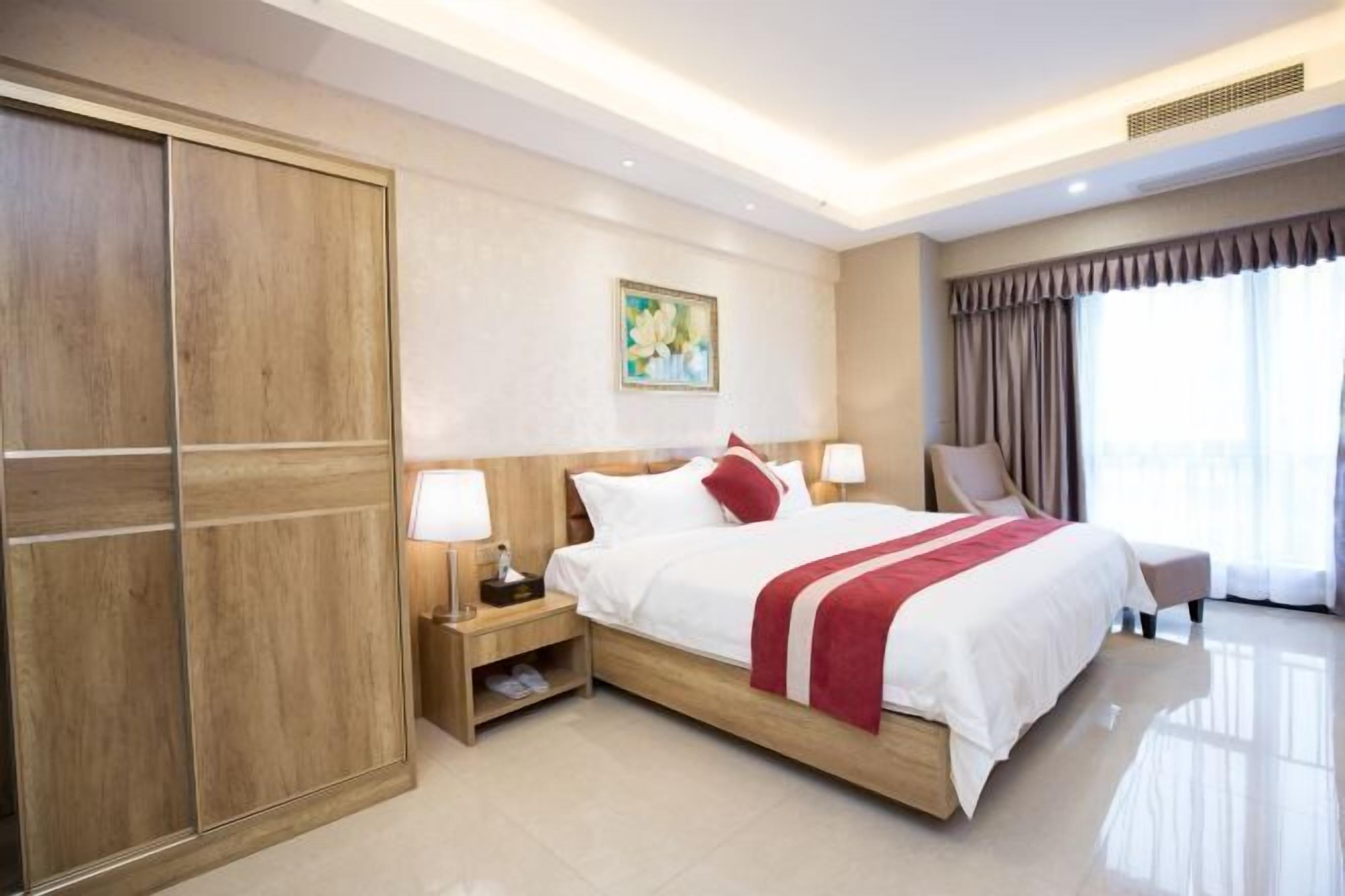 Une chambre d’hôtel avec un grand lit, une armoire en bois, des tables de chevet et une grande fenêtre avec des rideaux.