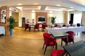 A spacious dining area with multiple tables and chairs, a kitchen in the background, and a large TV screen. - Marco Polo Hotel (Jiangmen Wanda Plaza) (Jiangmen)