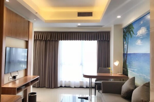 A modern living room with a flat-screen TV, a wooden entertainment unit, a glass coffee table, a sofa, a dining table with chairs, and a large window with curtains. - Marco Polo Hotel (Jiangmen Wanda Plaza) (Jiangmen)