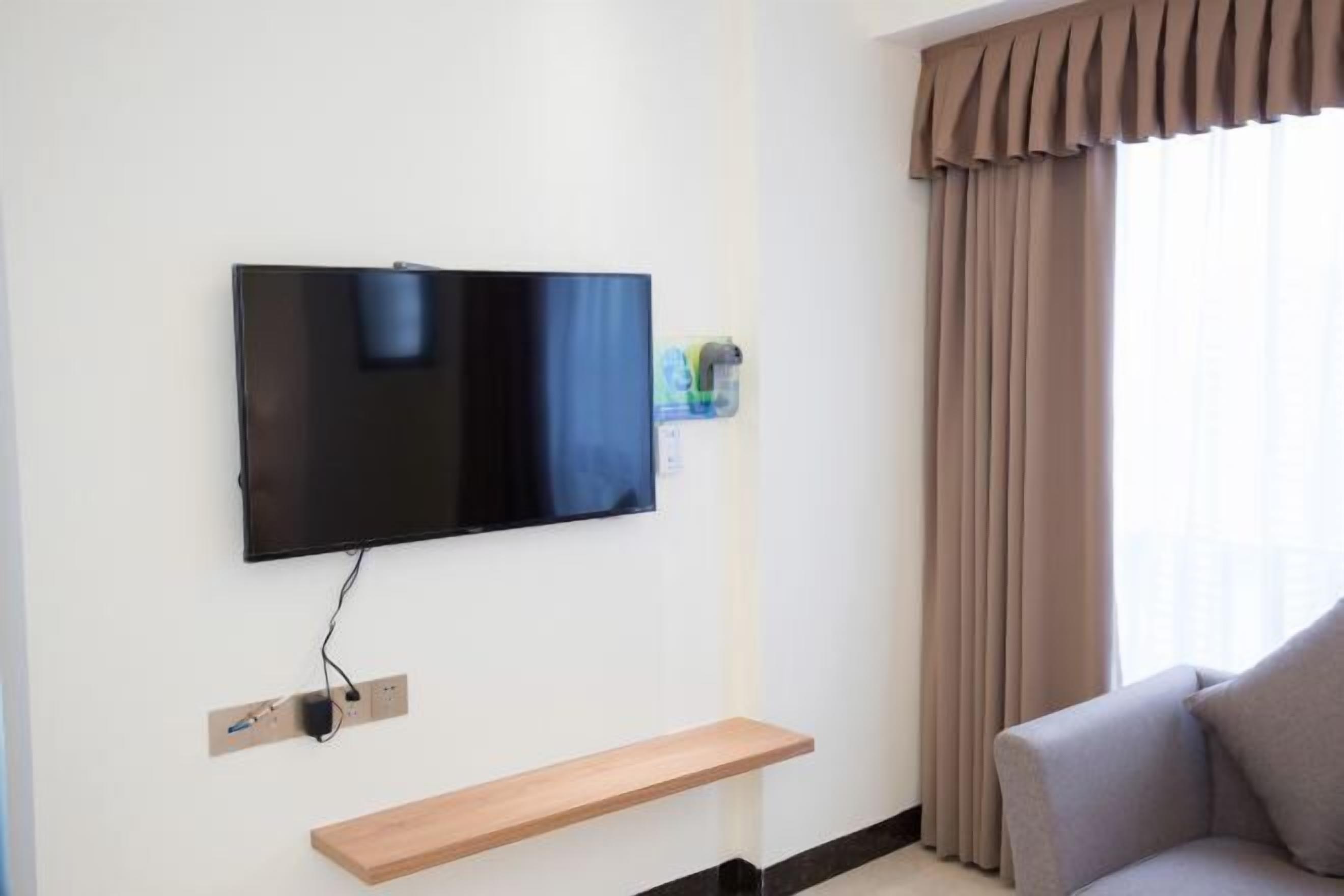 A modern living room with a flat-screen TV mounted on the wall, a wooden shelf below, and a grey sofa.