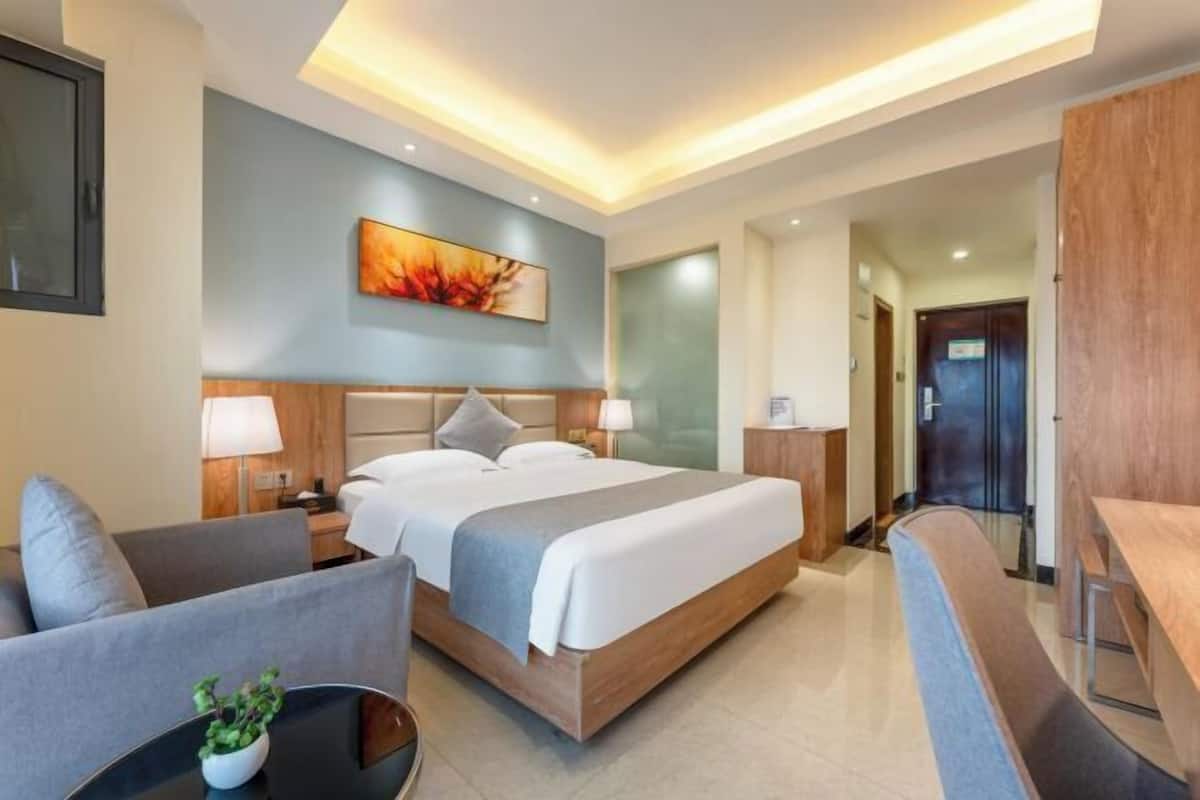 A modern hotel room with a large bed, a desk, a chair, and a small table with a plant.