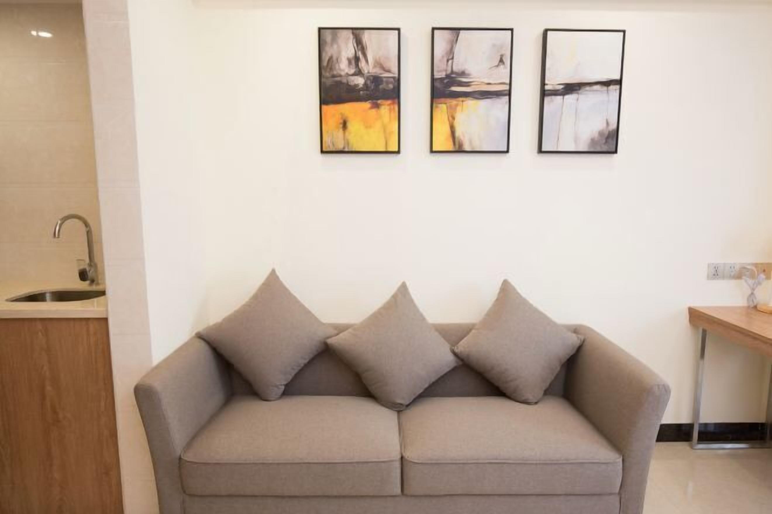 A neutral-toned sofa with three cushions in a modern, minimalistic room with a white wall and a wooden cabinet.