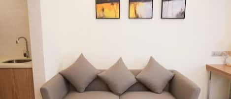 A neutral-toned sofa with three cushions in a modern, minimalistic room with a white wall and a wooden cabinet.