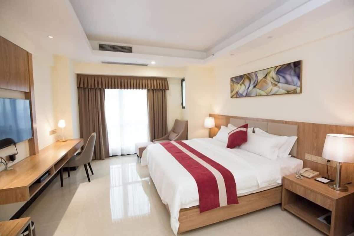 A hotel room with a bed, desk, chair, bedside table, and artwork on the wall.