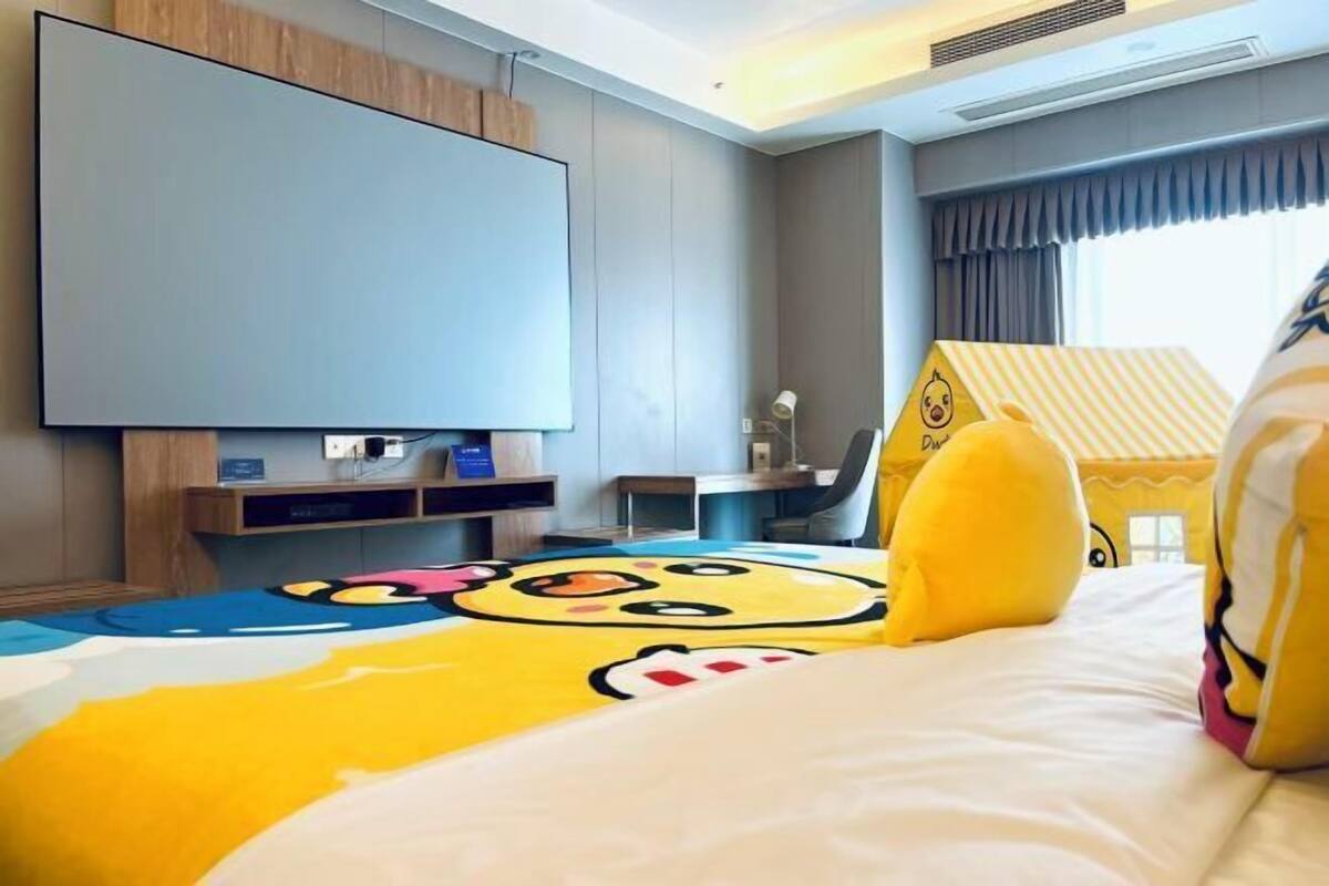 A hotel room with a bed, a flat-screen TV, a desk, and a window with curtains.