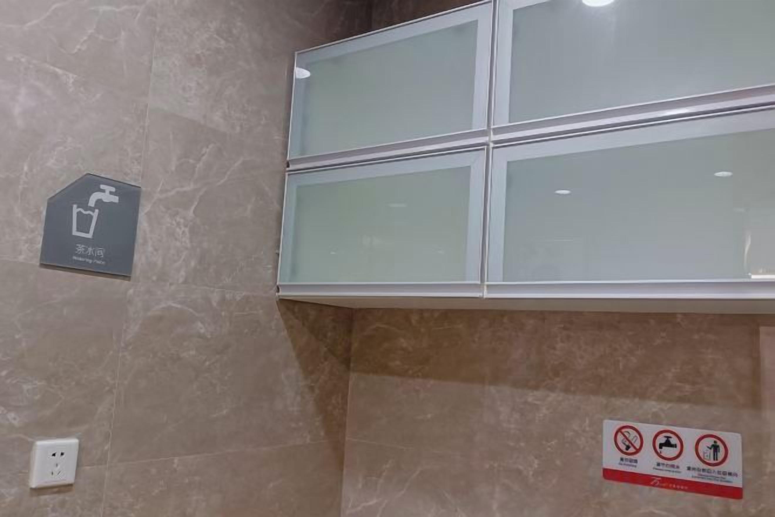 A bathroom with a marble wall, a glass shower enclosure, a handwashing station, and a no-smoking sign.