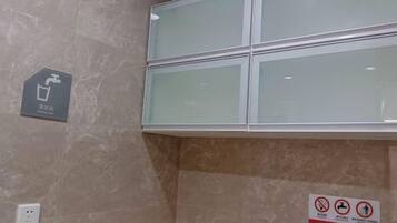 A bathroom with a marble wall, a glass shower enclosure, a handwashing station, and a no-smoking sign.