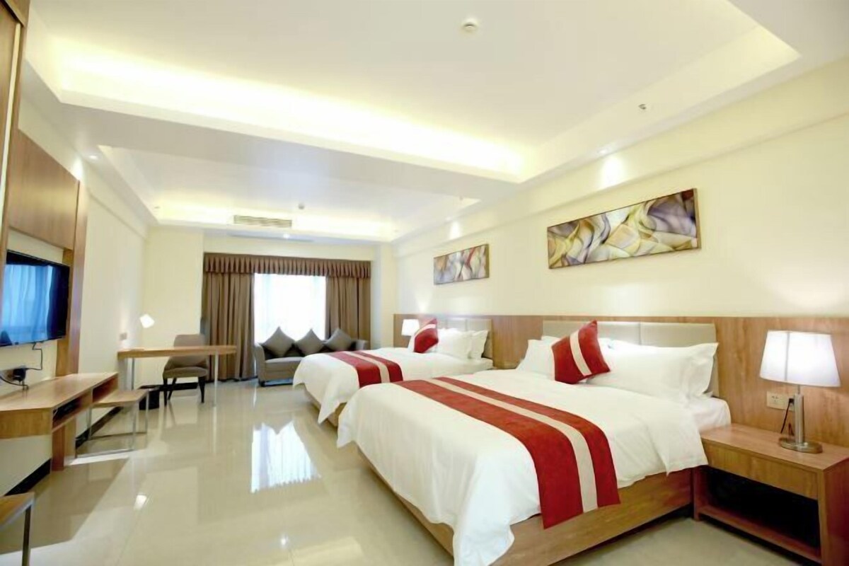 A hotel room with two beds, a desk, a TV, and artwork on the walls.