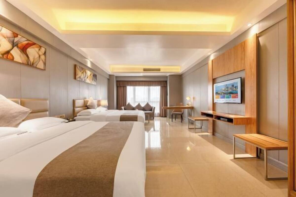 A hotel room with two beds, a desk, a TV, and artwork on the walls.