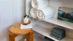 A neatly arranged shelf with folded towels, a small table with a plant, and a decorative vase.