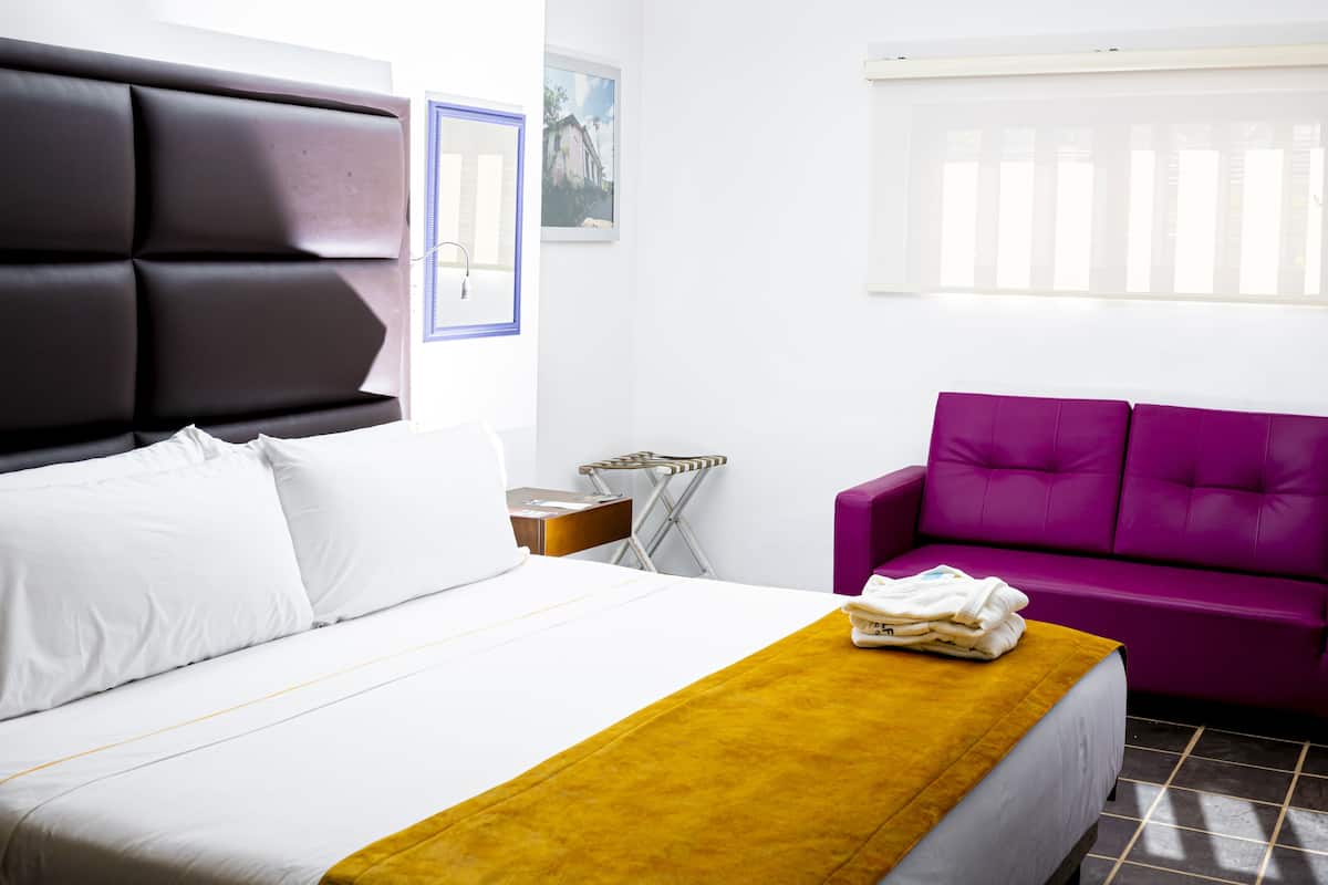Habitación de hotel con cama, sofá púrpura, una mesita y ventana con persianas.