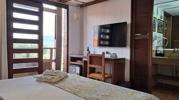 Un dormitorio con cama, televisor montado en la pared, escritorio con silla y baño con lavamanos y espejo.