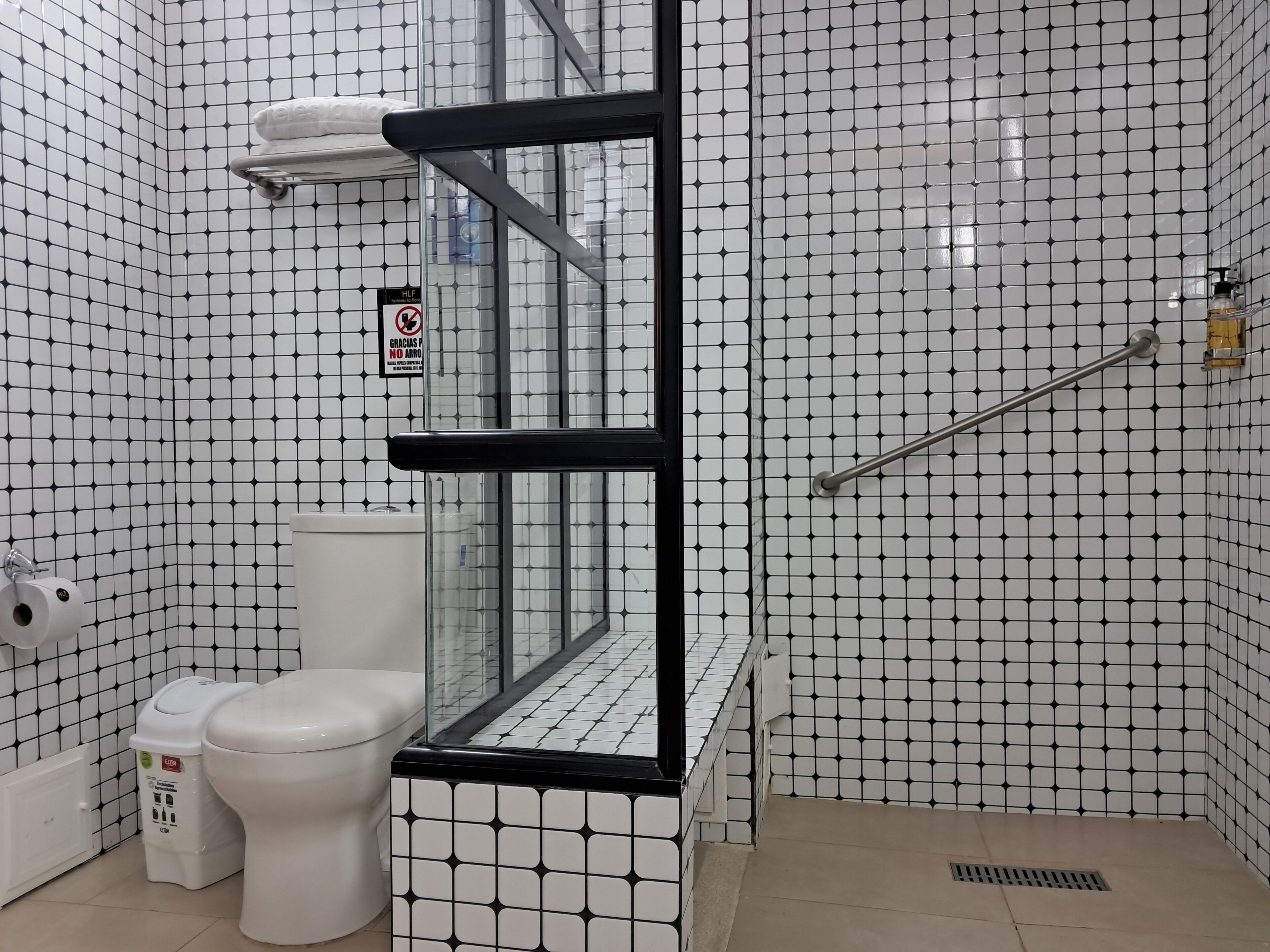 A bathroom with a toilet, a trash bin, and a glass-enclosed shower area.