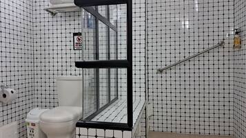 A bathroom with a toilet, a trash bin, and a glass-enclosed shower area.