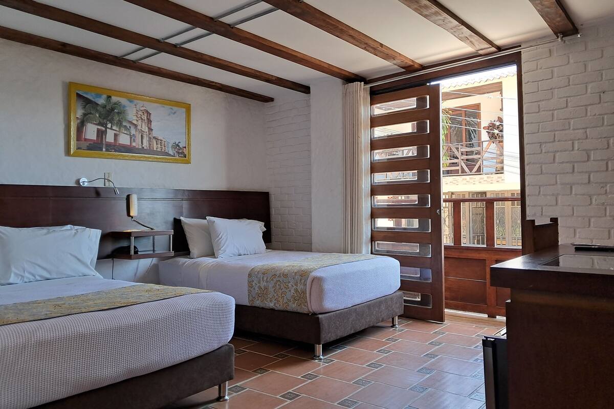 Habitación de hotel con dos camas, cabecero de madera, un cuadro en la pared y vistas a través de una puerta de madera.