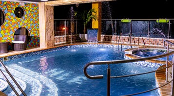 Una piscina con borde de azulejos, una zona de estar con sillas y una pared decorativa con diseño de mosaico.