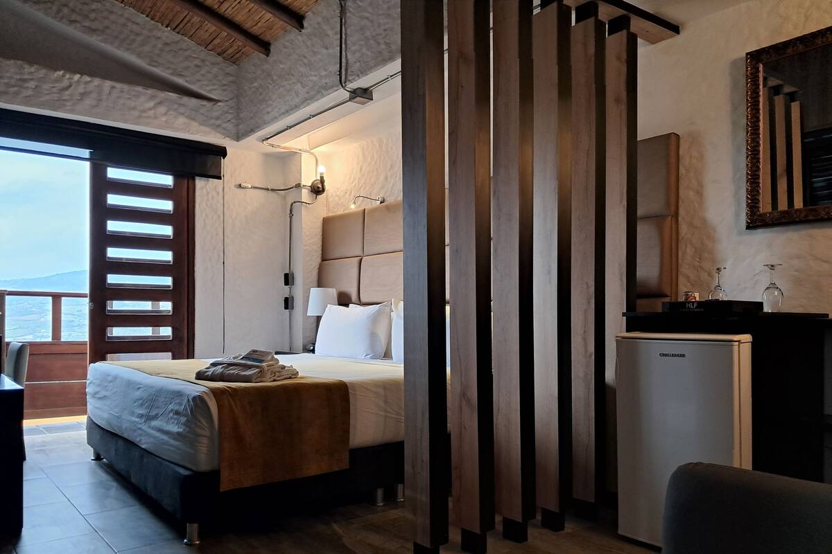 Una habitación de hotel con cama, mesita de noche, lámpara y minibar.