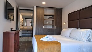 Een hotelkamer met een bed, een houten bankje, een bureau, een spiegel en een kledingkast.