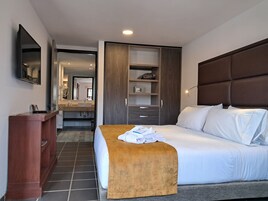 Una habitación de hotel con cama, un banco de madera, un escritorio, un espejo y un armario.
