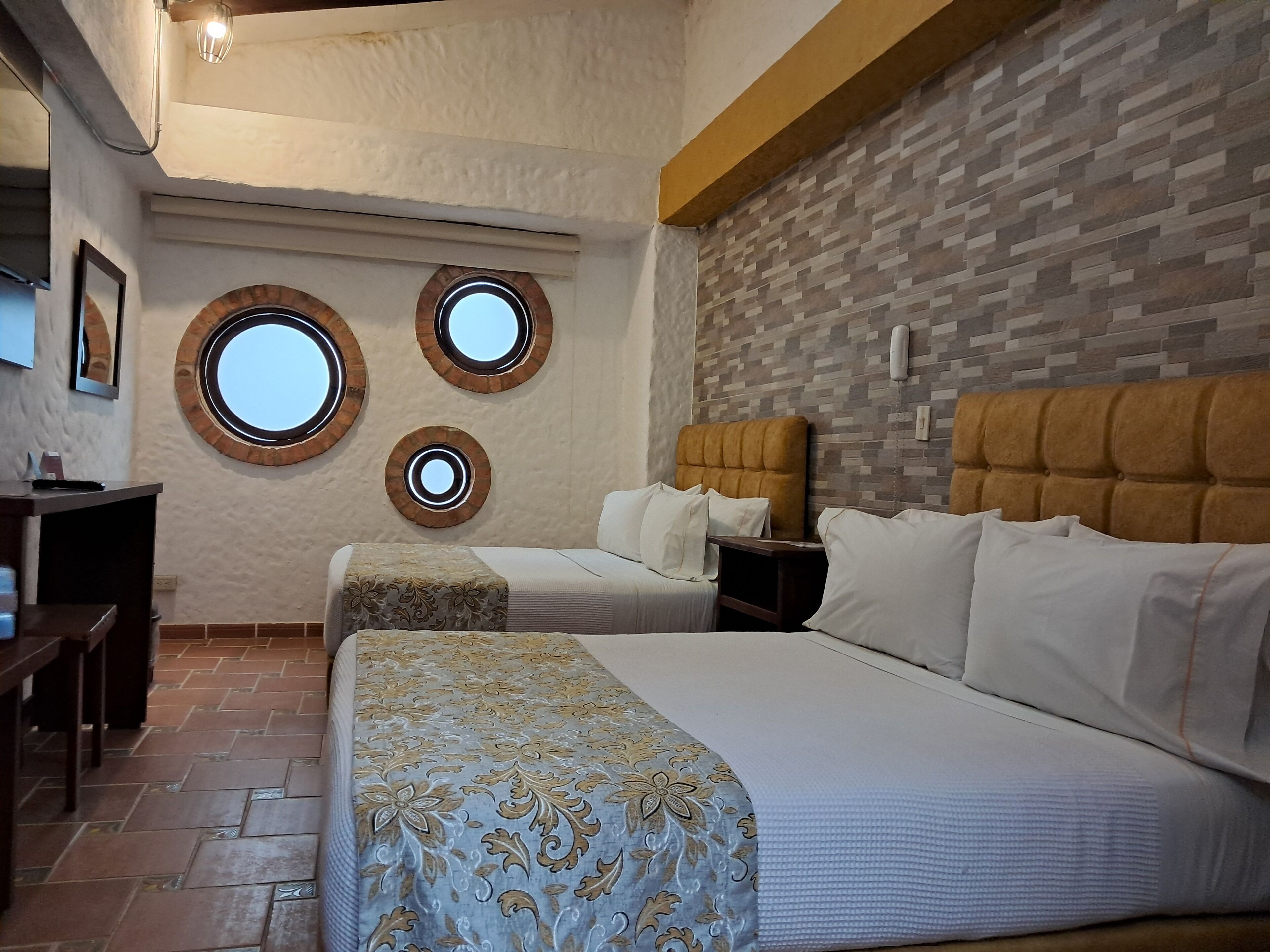 A hotel room with two beds, a wooden headboard, a brick wall, and a tiled floor.