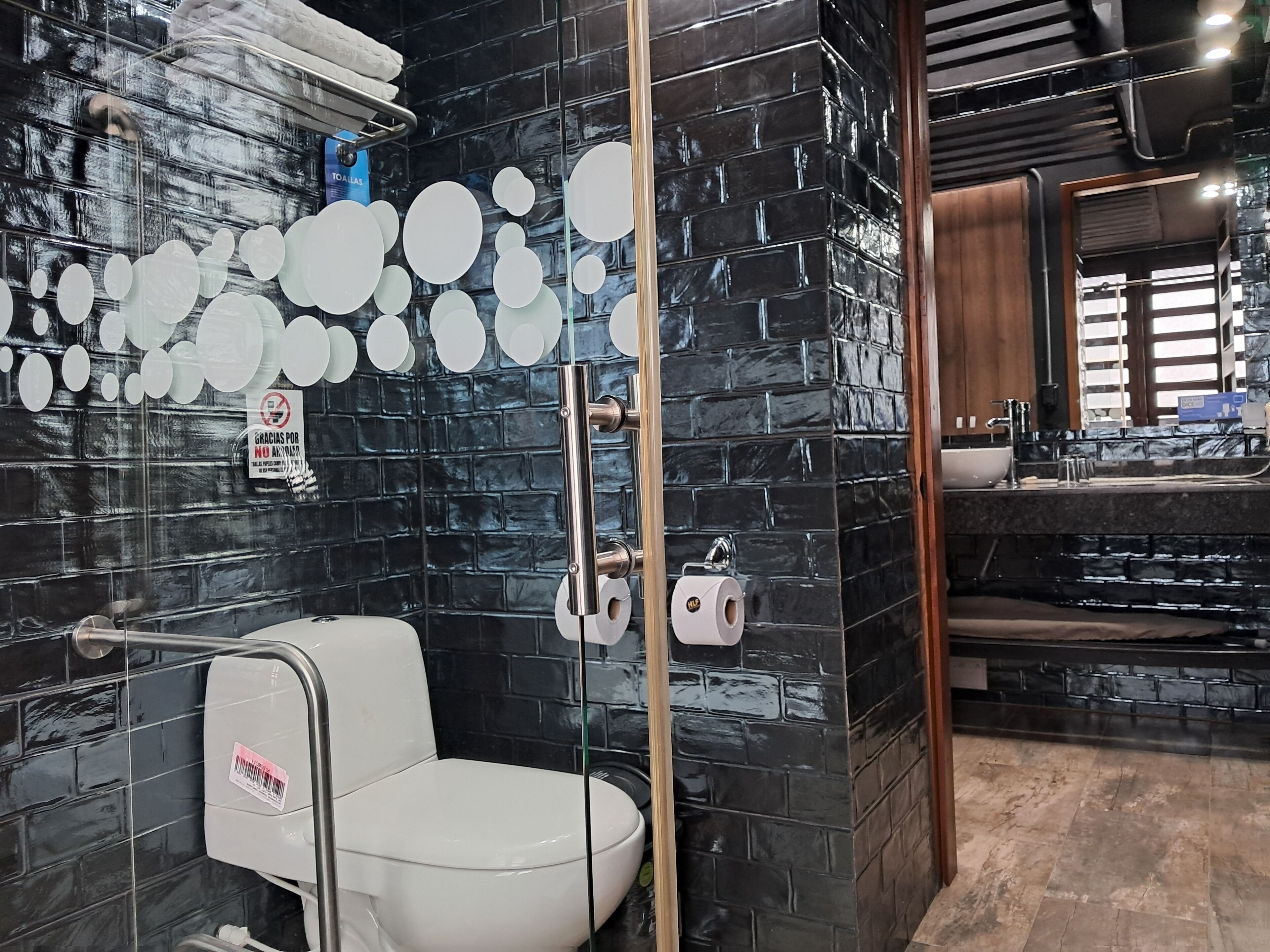 Une salle de bain moderne avec un mur en briques noires, des toilettes blanches et une cabine de douche en verre.