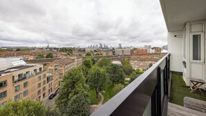 Un balcón con vista a un paisaje urbano, que incluye edificios y árboles.