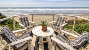 Eine Terrasse mit vier Stühlen und einem Tisch, mit Blick auf einen Strand.