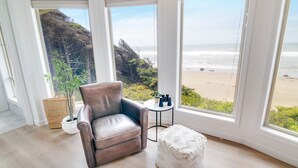 Ein Zimmer mit Ledersessel, einem kleinen runden Tisch mit Fernglas und Blick auf den Strand.